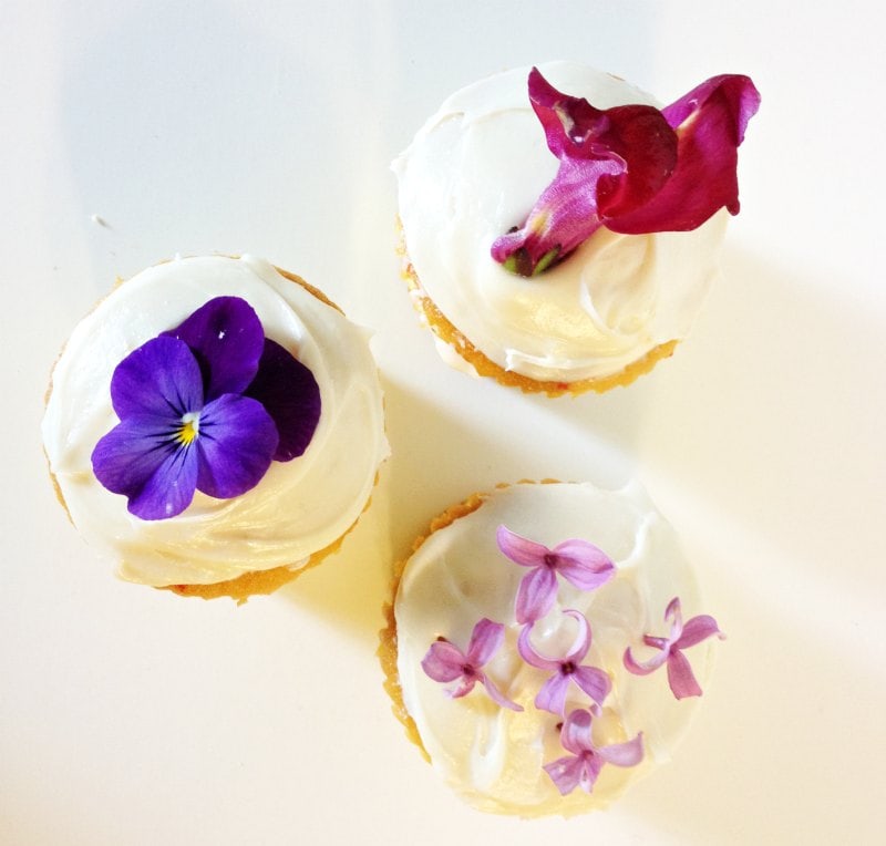 Cupcakes topped with pansies, lilac blossoms and snapdragon flower.