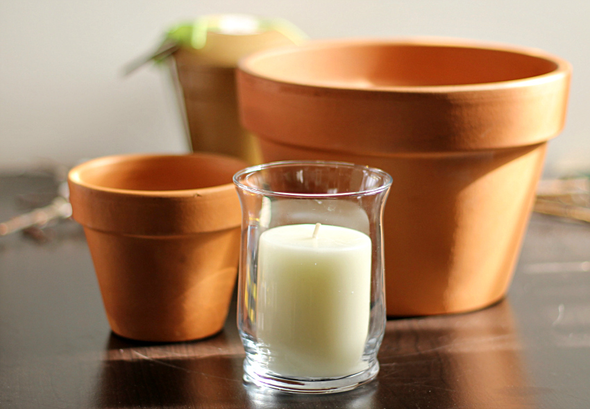 Large clay pot, small clay pot and a small pillar candle in a glass vase.
