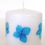 Small white pillar candle with blue pressed flowers.