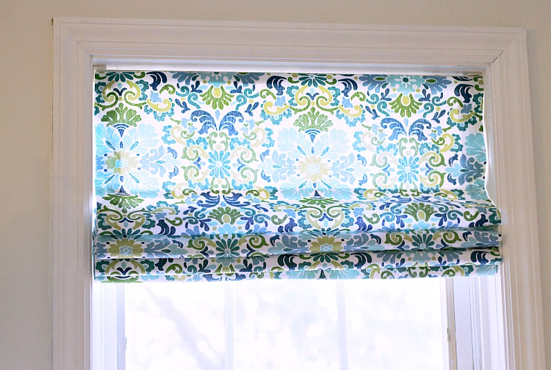 Shades of blue and green fabric Roman mini blind handing in a window.