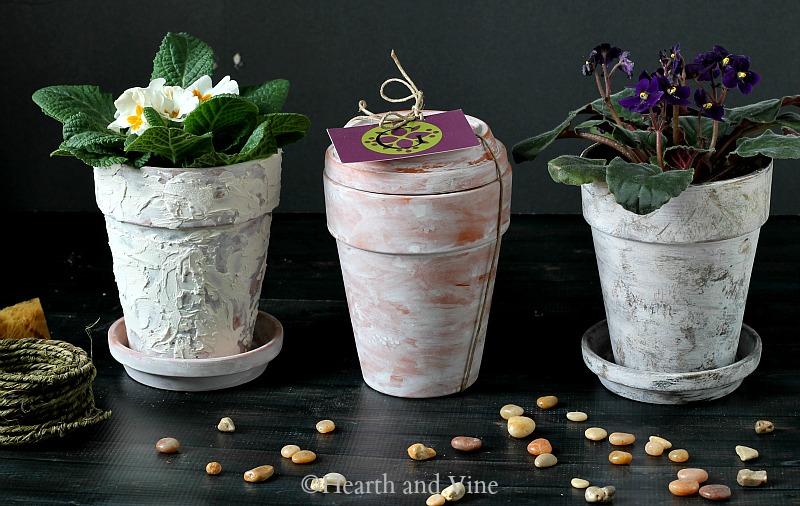 Aged terra cotta pots with flowers in top and one with a saucer on top.