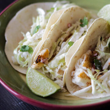 Three fish tacos with slaw and a lime wedge
