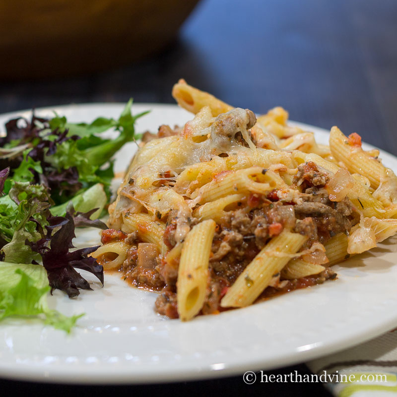 Serving of spaghetti casserole with salad on a white plate.