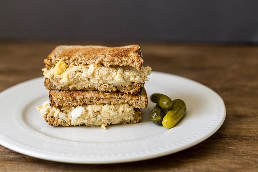 Tuna egg sandwich with dill pickles on the side.
