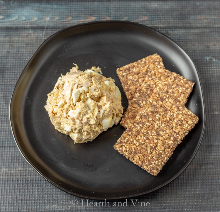 A scoop of tuna salad with eggs and crackers on a plate.