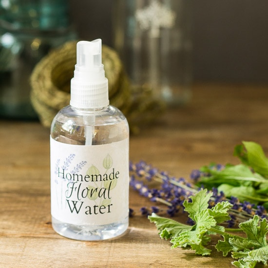 Homemade floral water spray bottle next to fresh lavender, rose scented geranium and mint leaves.