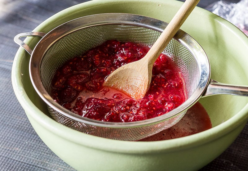 Straining berries in a mesh strainer with a wooden spoon.