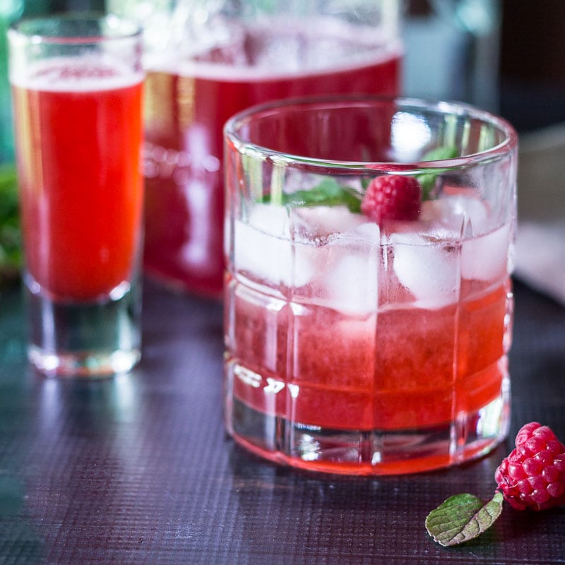 Raspberry shrub in a glass with mint and fresh rapberries.