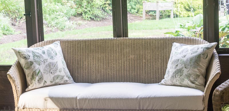 Two leaf printed pillows on a couch on an outdoor porch.