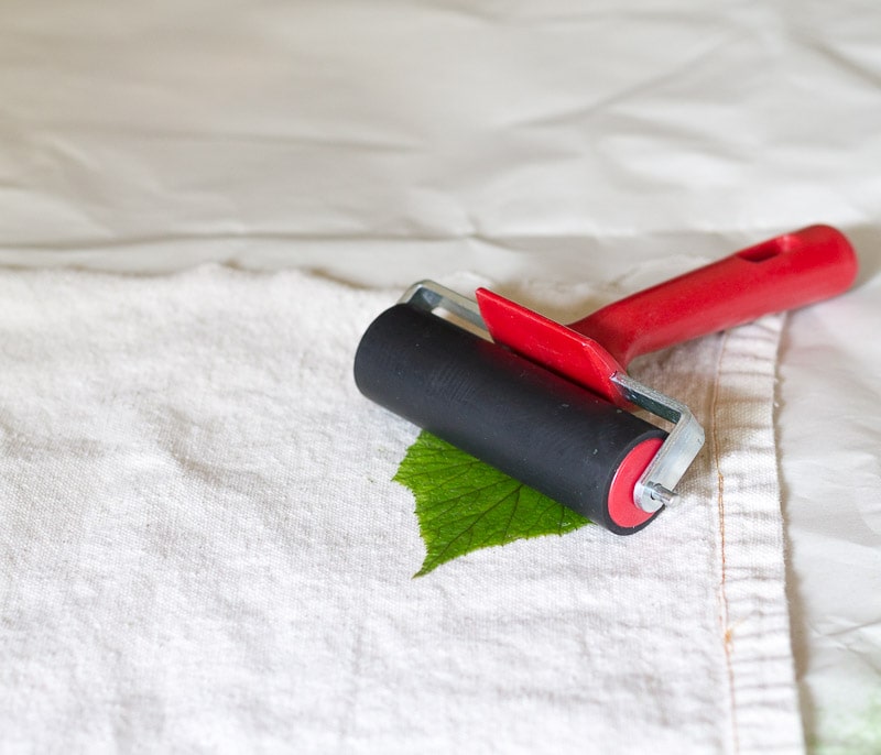 Red brayer rolling on leaf on drop cloth fabric.