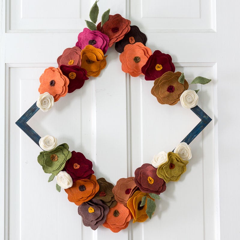 Felt flower wreath in fall colors on a blue diamond shaped frame.