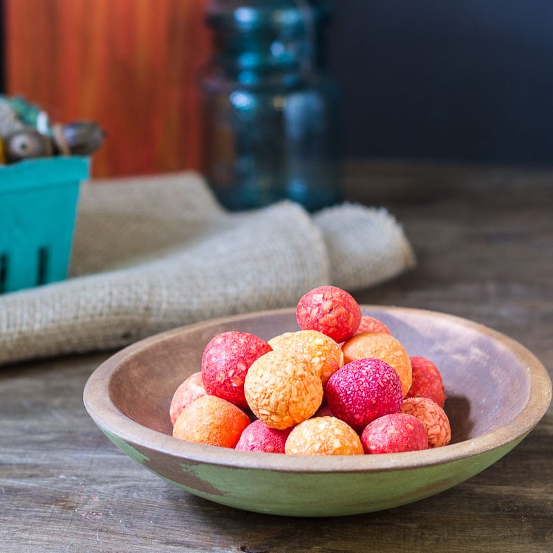 Orange and red small soap balls in a wooden dish.