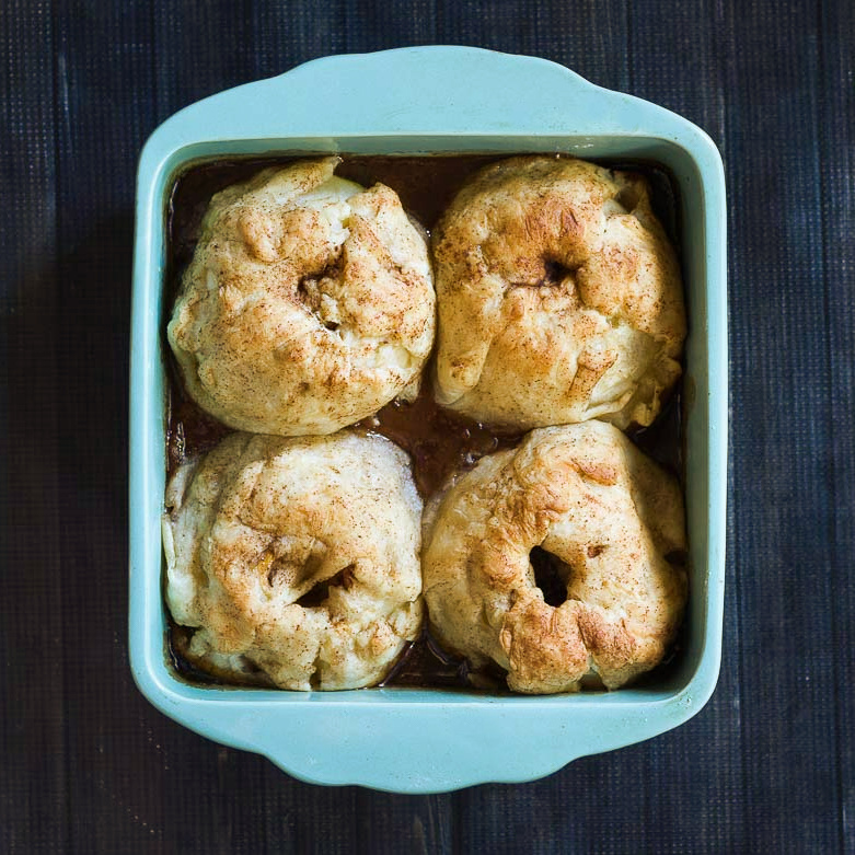 Four apple dumplings in a blue baking dish