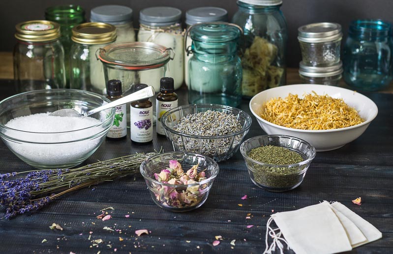 bowls of herbs and bath salts, bottles of essential oils and different sizes of mason jars and other jarbs.