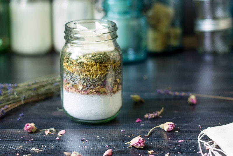 Herbal bath salts in a pint mason jar with scattered dried rosebud and lavender on the table.