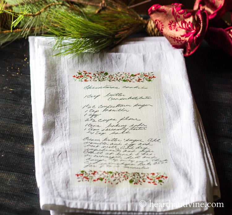 Family cookie recipe on a white tea towel with faux pine and a red ribbon around it.