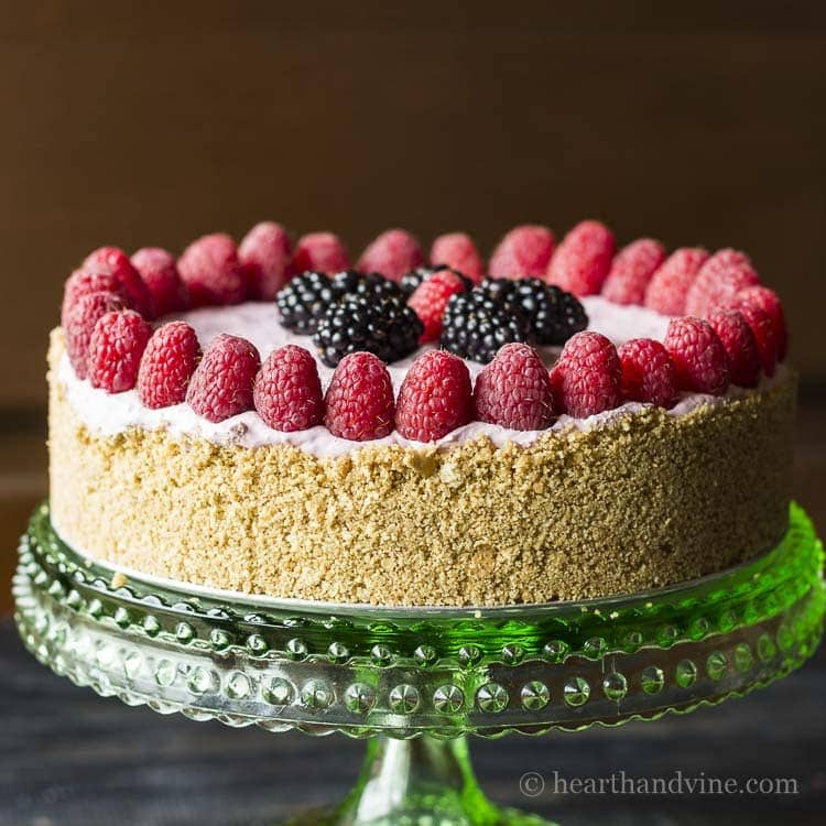 Blackberry and raspberry no sugar cheesecake with graham cracker crust on a green glass pedestal.
