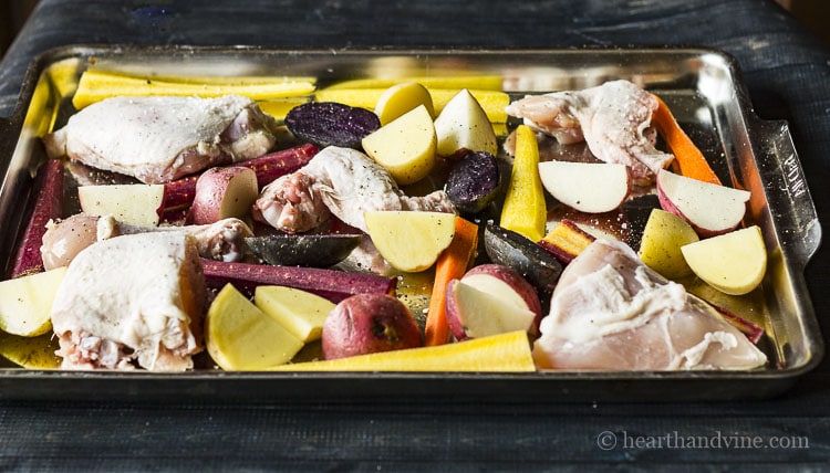 chicken parts, potatoes and tri-colored carrots on sheet pan.