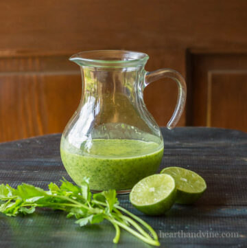 Pitcher of cilantro lime vinaigrette with some fresh cilantro cuttings and a cut open lime.