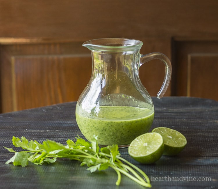 Cilantro lime vinaigrette in a small pitcher with limes and cilantro on the side.