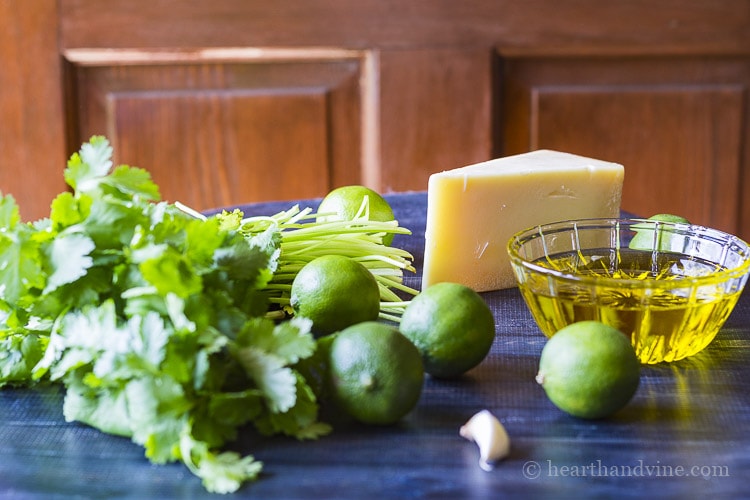 Ingredients for cilantro lime vinaigrette including a wedge of Parmesan cheese, limes, cilantro, oil and garlic.