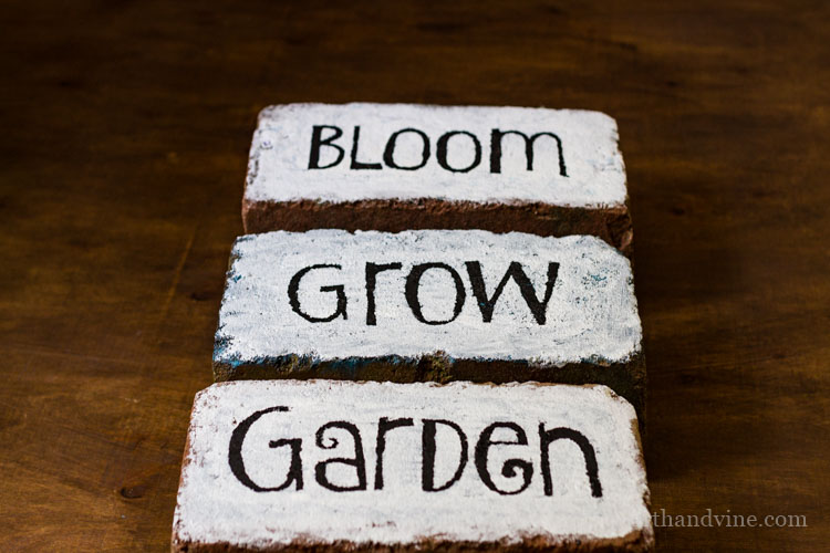 Three bricks with white paint and black letters spelling the words bloom, grow, and garden.