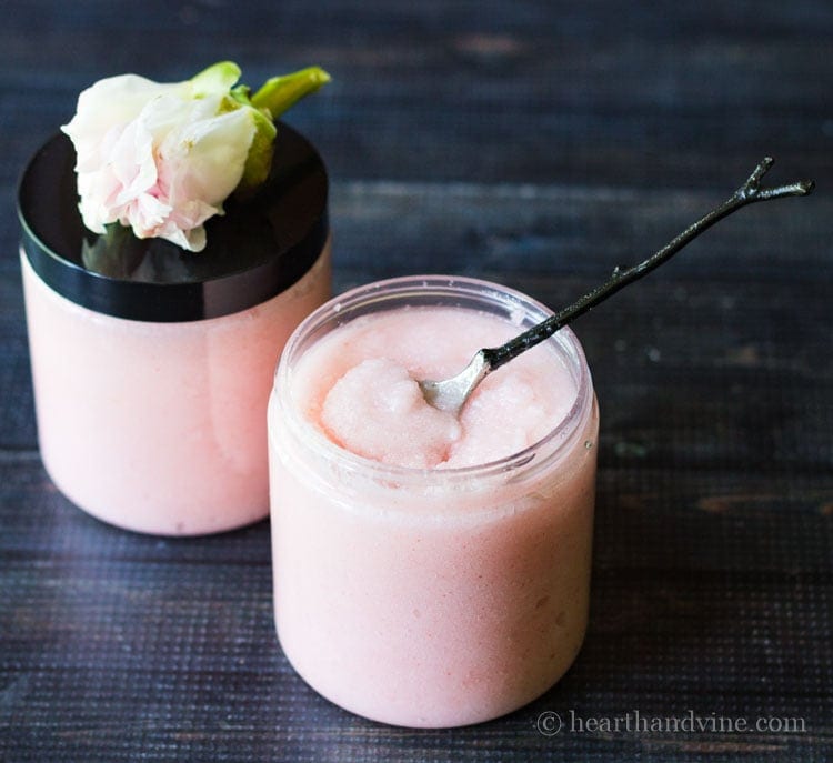 Open jar of blush pink sugar body scrub with a tiny spoon.