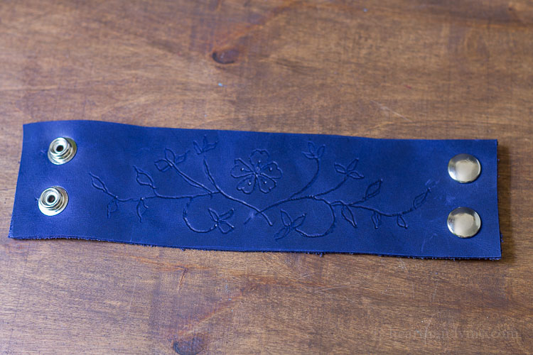 Blue leather strip with floral pattern engraved and two metal snaps to form bracelet.