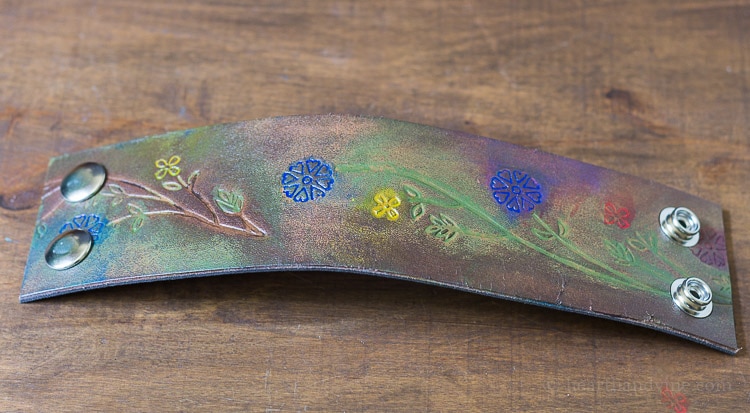 Floral engraved belt cut for wrist cuff  with snaps and leather ink embellishment.