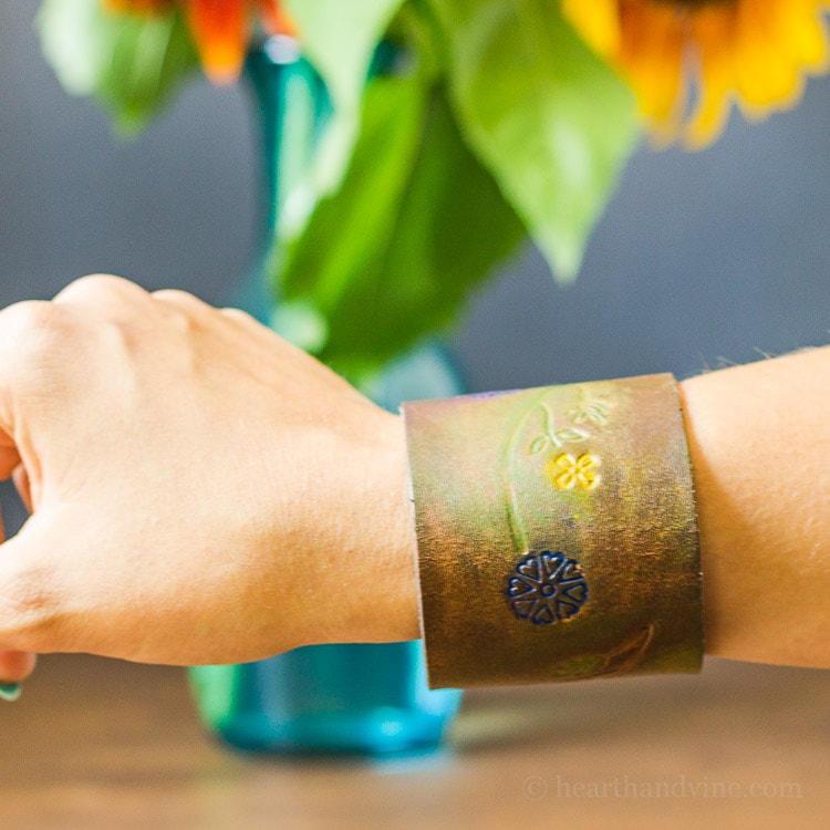 Brown leather cuff with colored floral engraving on wrist.
