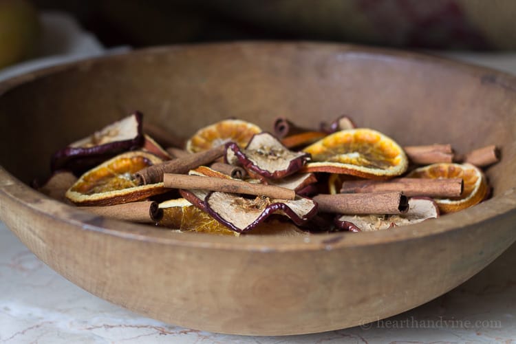 Homemade natural potpourri made with natural apples, orange slices and cinnamon sticks in a large wooden bowl.