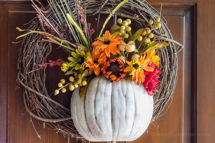 A pumpkin wreath made with half a pumpkin that acts as a vase for faux flowers is a great way to add beautiful fall color to your front door.