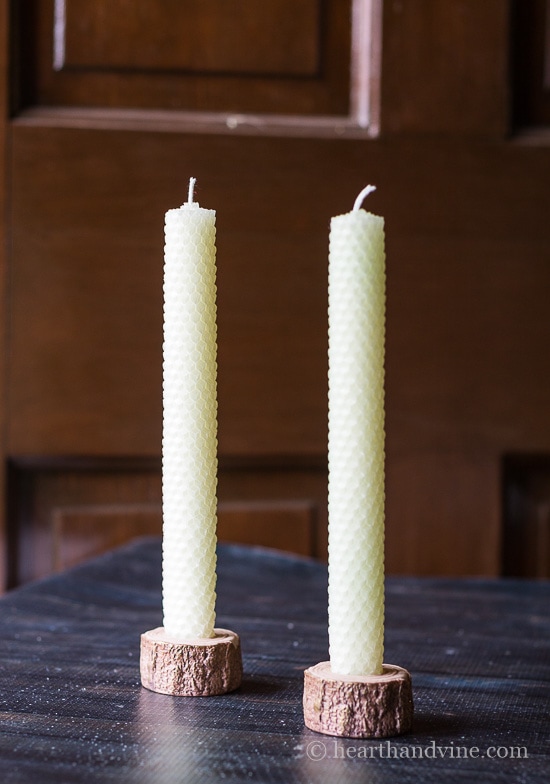 Two natural colored rolled beeswax candles in small wooden holders.