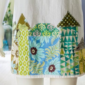 Tea towel aprons are super simple to make. This one is decorated with whimsical fabric houses appliqued at the bottom for a fun look.