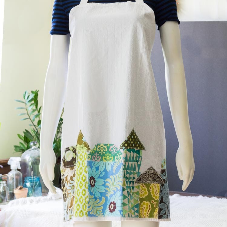 Tea towel aprons are super simple to make. This one is decorated with whimsical fabric houses appliqued at the bottom for a fun look.