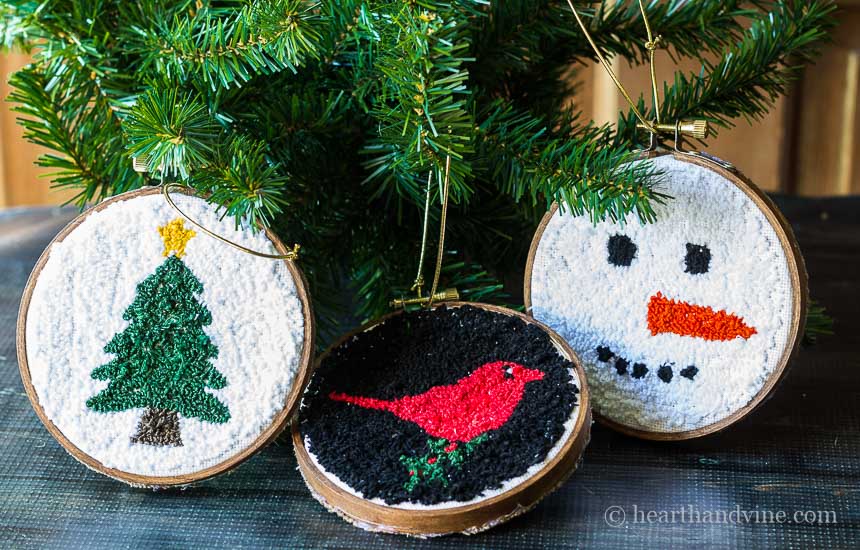 Three punch ornaments next to a fake tree. One is a snowman face, one a red bird and the 3rd is a Christmas tree with a gold star.
