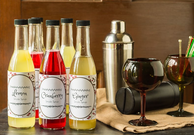 Simple syrups bottles in lemon, cranberry and ginger next to some barware and accessories.