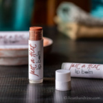A tube of tined lip balm with the cap off standing up next to one on its side.