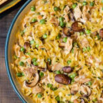Large serving bowl with a noodle and turkey casserole with mushrooms and peas.