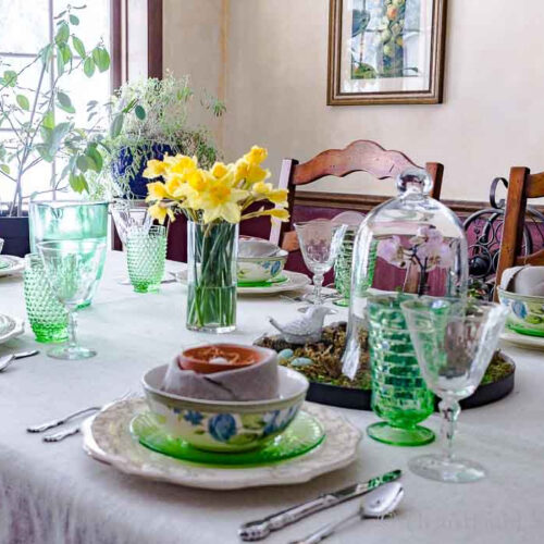 Partial view of a spring tablescape with a cloche and daffodil centerpiences.