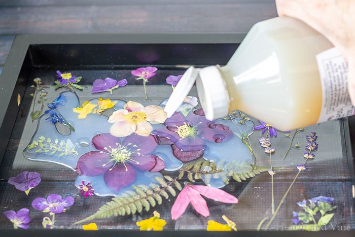 Pouring on liquid glass onto pressed flowers on tray.