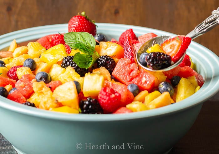 Spoon of fruit salad with ginger lime mint dressing mix in.