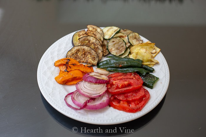 Grilled sliced vegetables including, red onions, tomatoes, orange peppers, eggplant, zucchini, and poblano peppers.