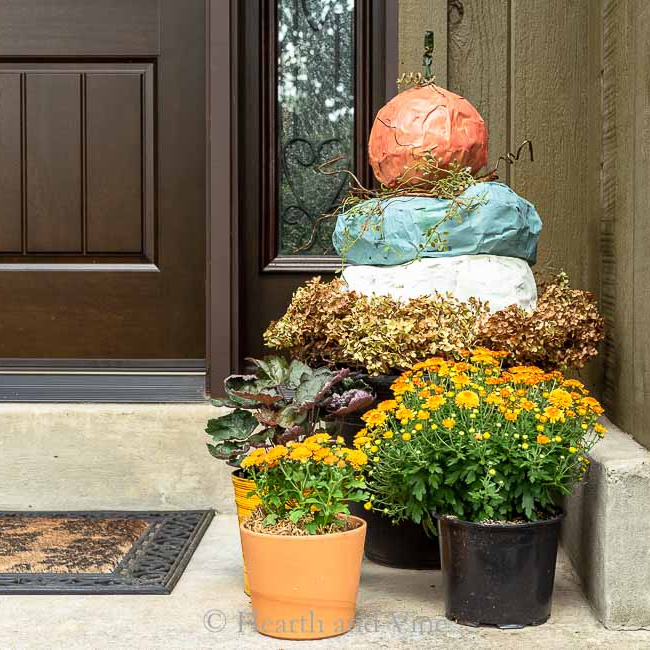 Paper mache pumpkin topiary behind pots of mums.