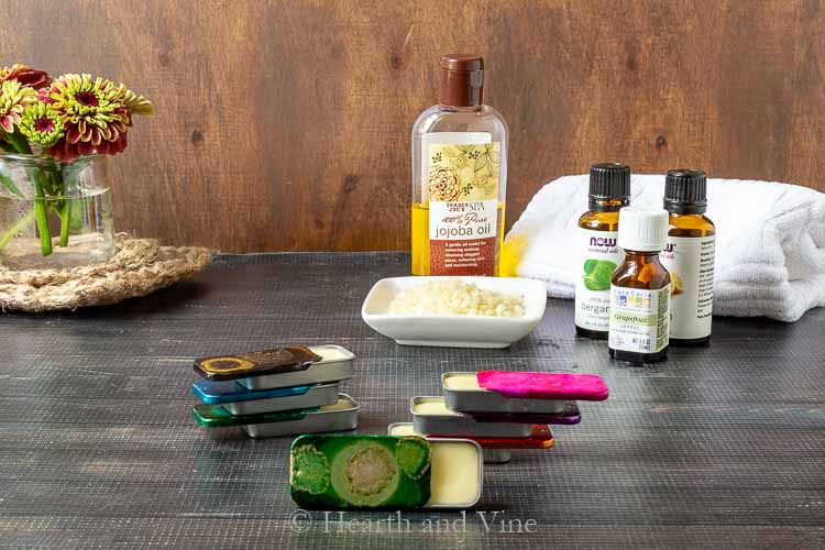 Solid perfume stack in front and a plate of beeswax pellets, jojoba oil and essential oils in the background.