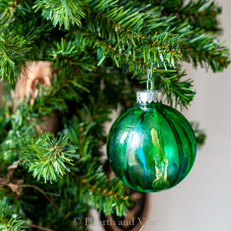 Green, blue and gold alcohol ink ornament on a tree.