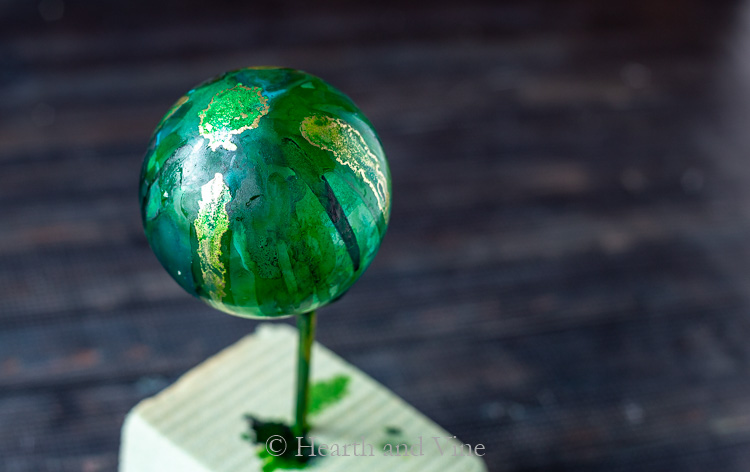 Alcohol ink ornament with the ink on the outside set on a stick in foam to dry.