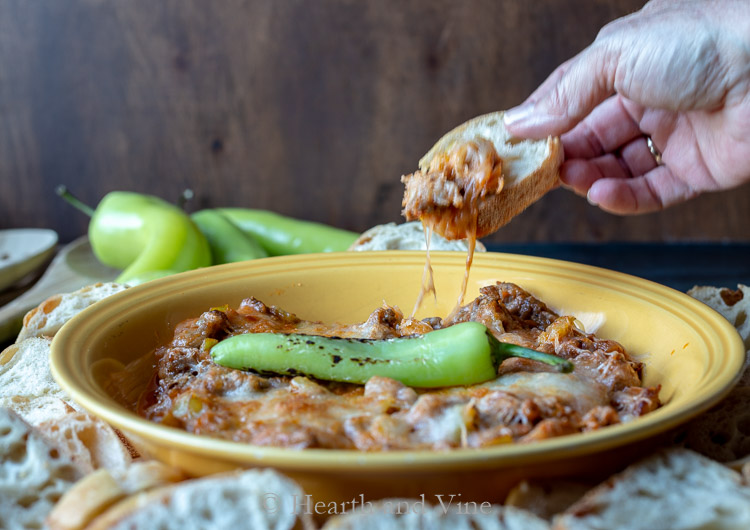 Hot banana pepper dip with a hand holding bread and dipping into the dish.
