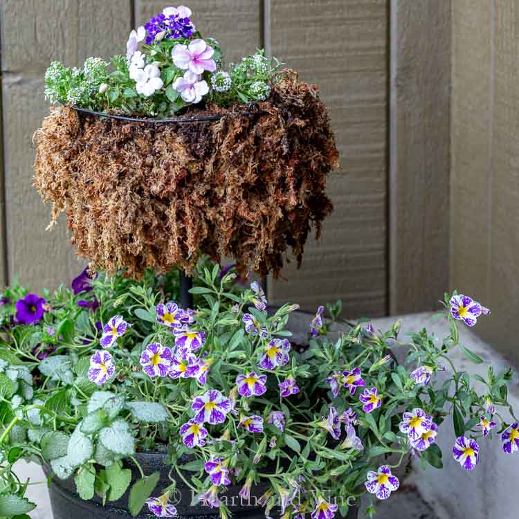 Shades of purple and pink annuals in a homemade tiered planter on a porch.