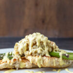 Side view of plated chicken oscar. Breaded chicken topped with asparagus, crabmeat and hollandaise sauce.